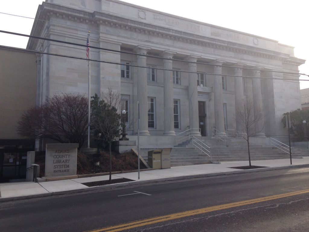 A large building with columns and stairs is on the side of the road