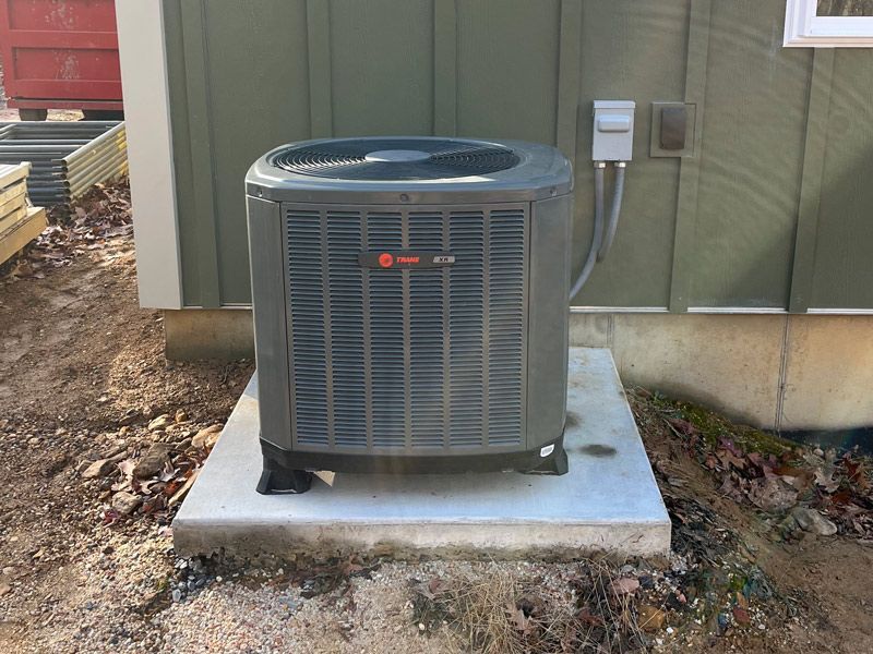 A gray air conditioner is sitting on a concrete platform in front of a green building.