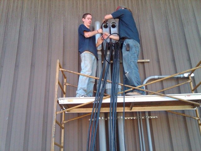 Two men standing on a scaffolding working on wires