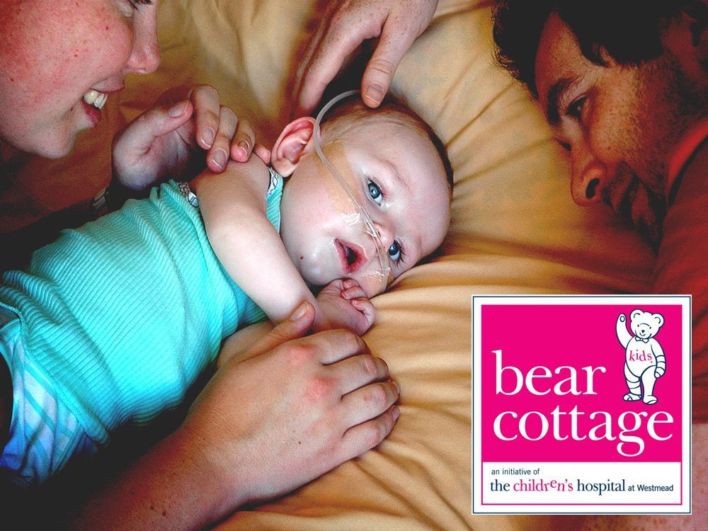 A baby is laying on a bed next to a bear cottage logo