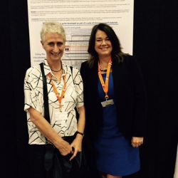 Two women are posing for a picture in front of a poster