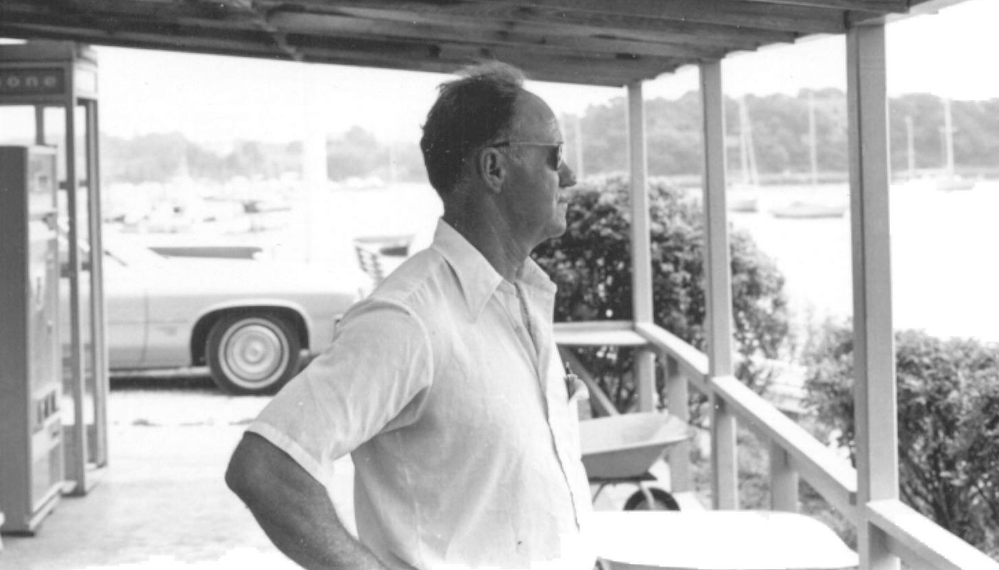 A man standing on a porch with a car in the background.