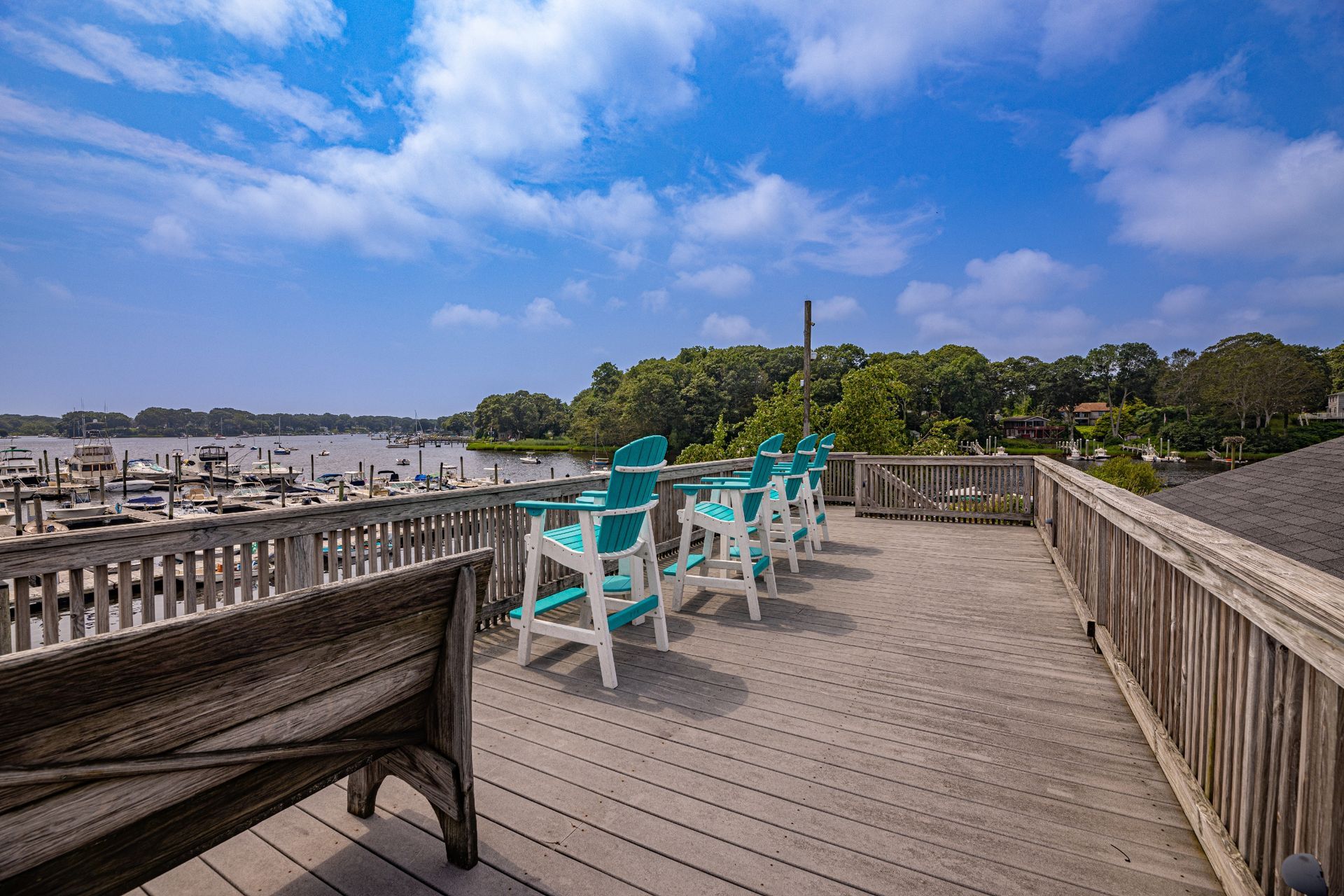 A wooden deck with chairs and a bench overlooking a body of water.