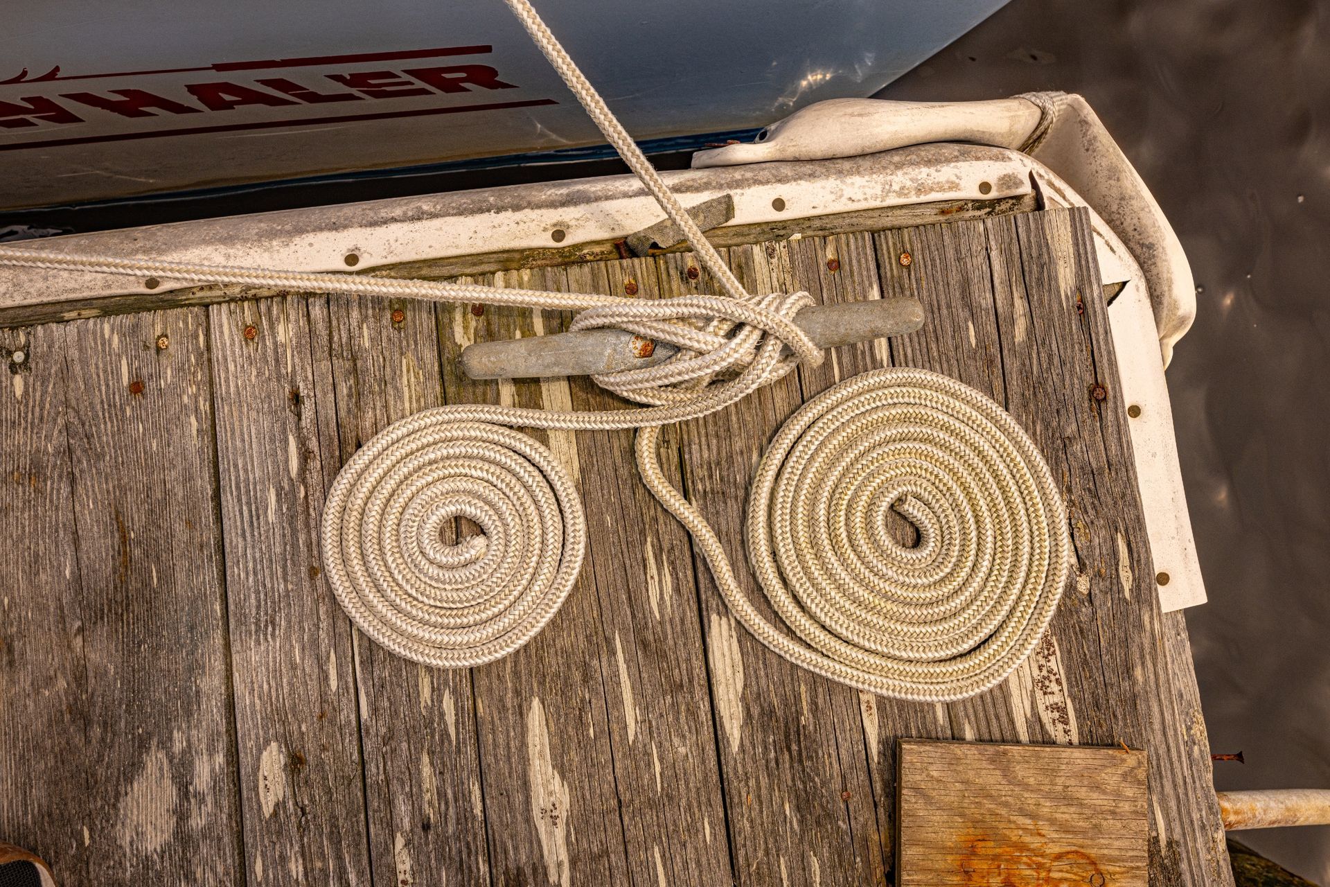 A wooden dock with ropes and a boat in the background
