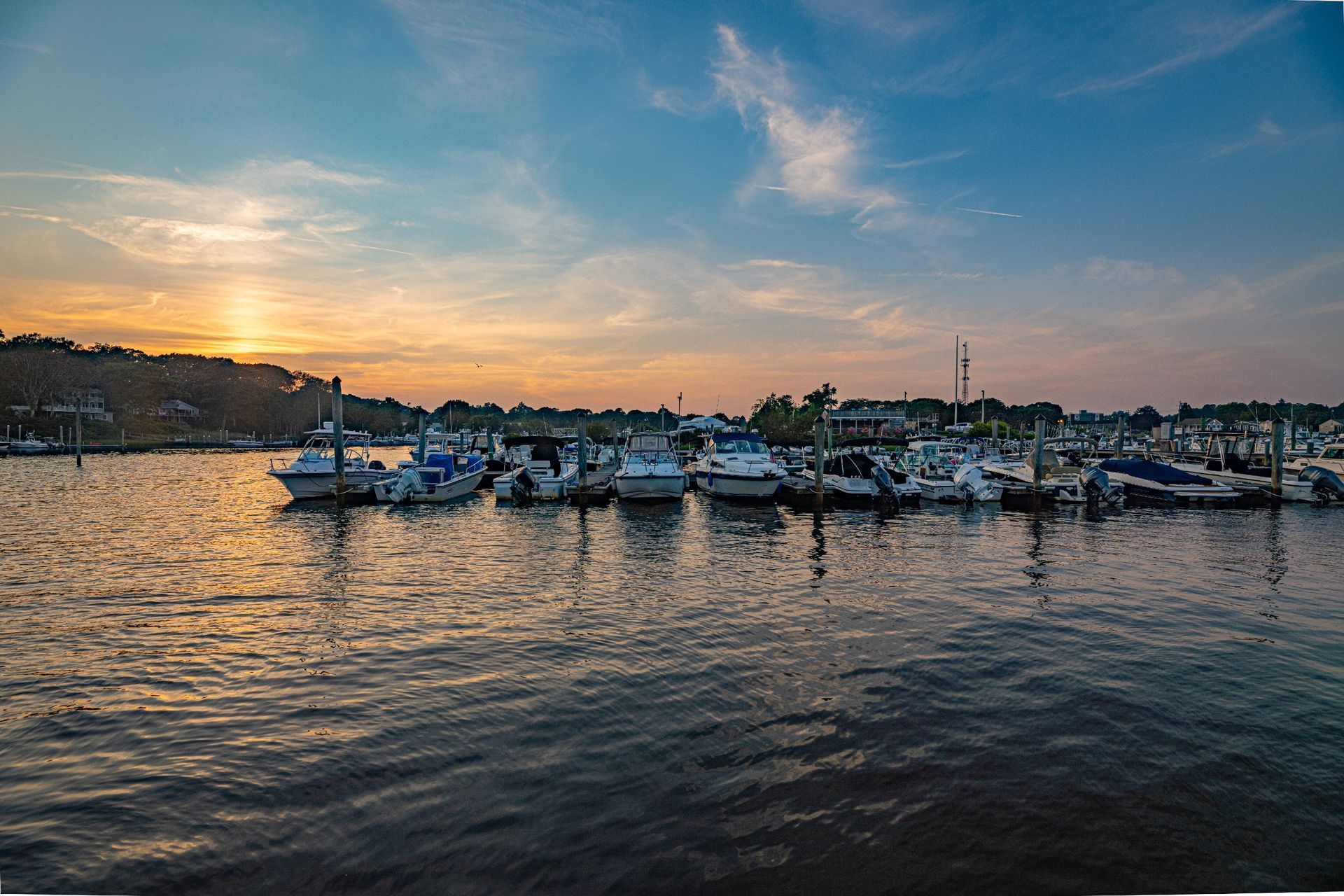 A row of boats are docked in a harbor at sunset.
