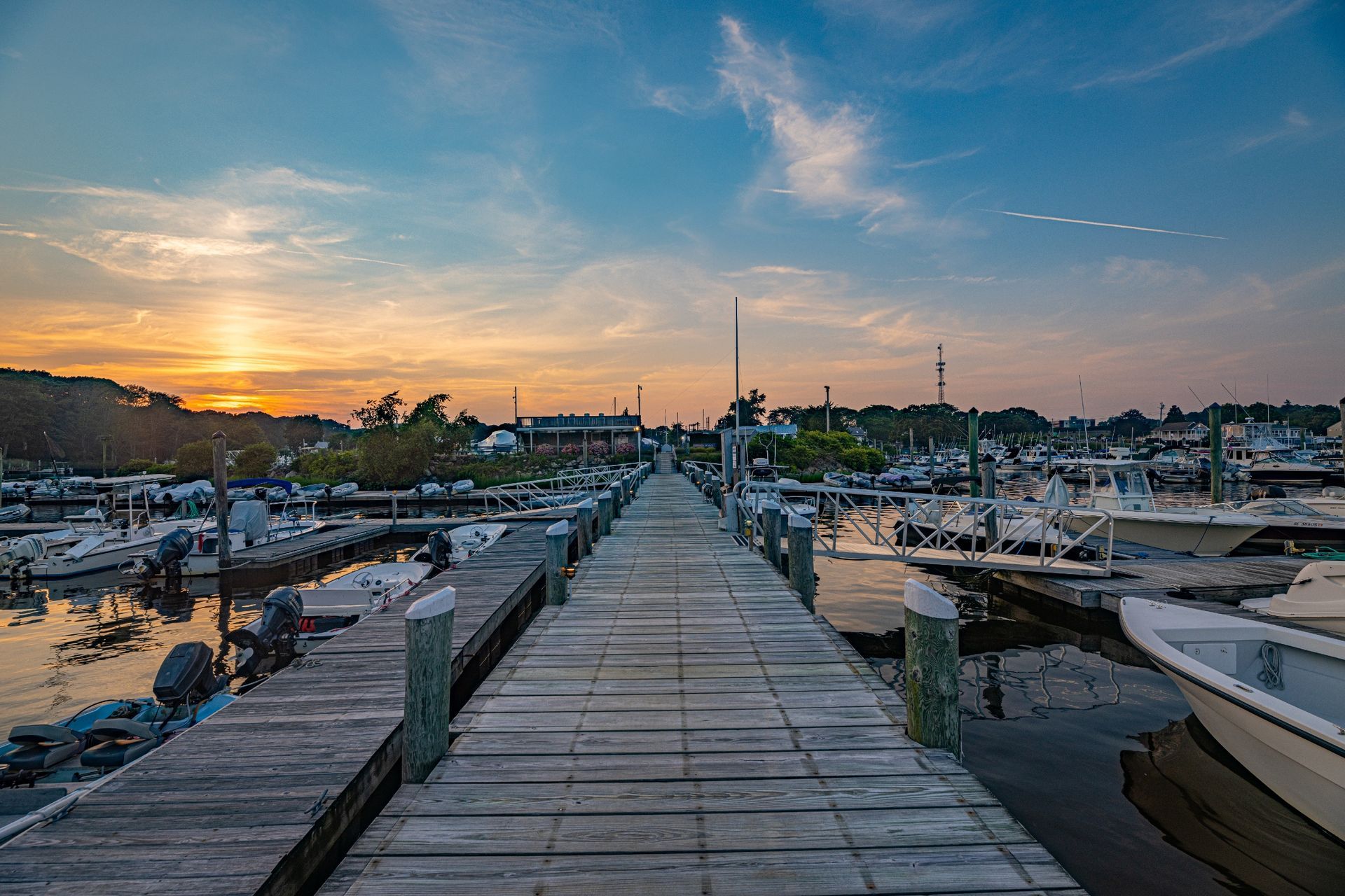 A long wooden dock with boats docked at a marina at sunset.