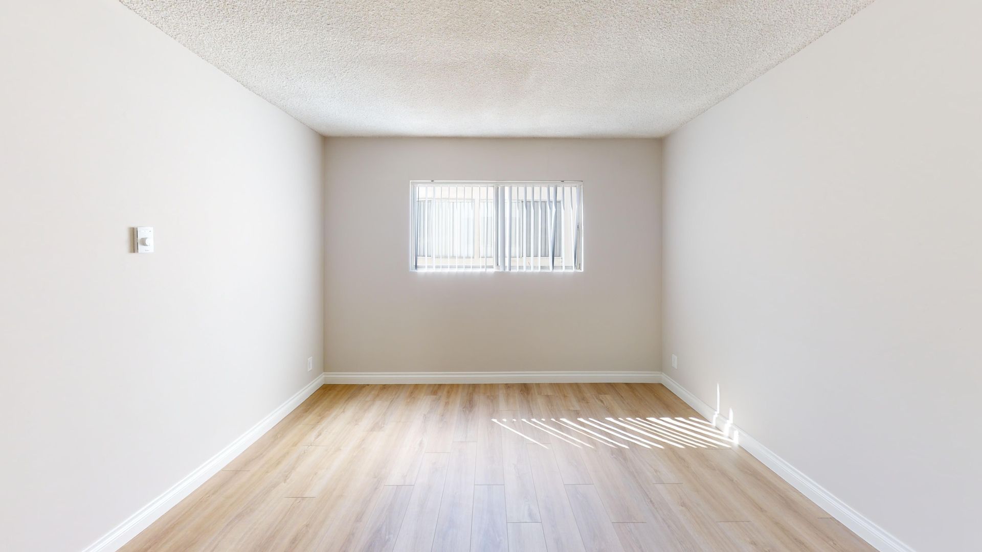 Empty room with a window, wood floor, and white walls and ceiling.