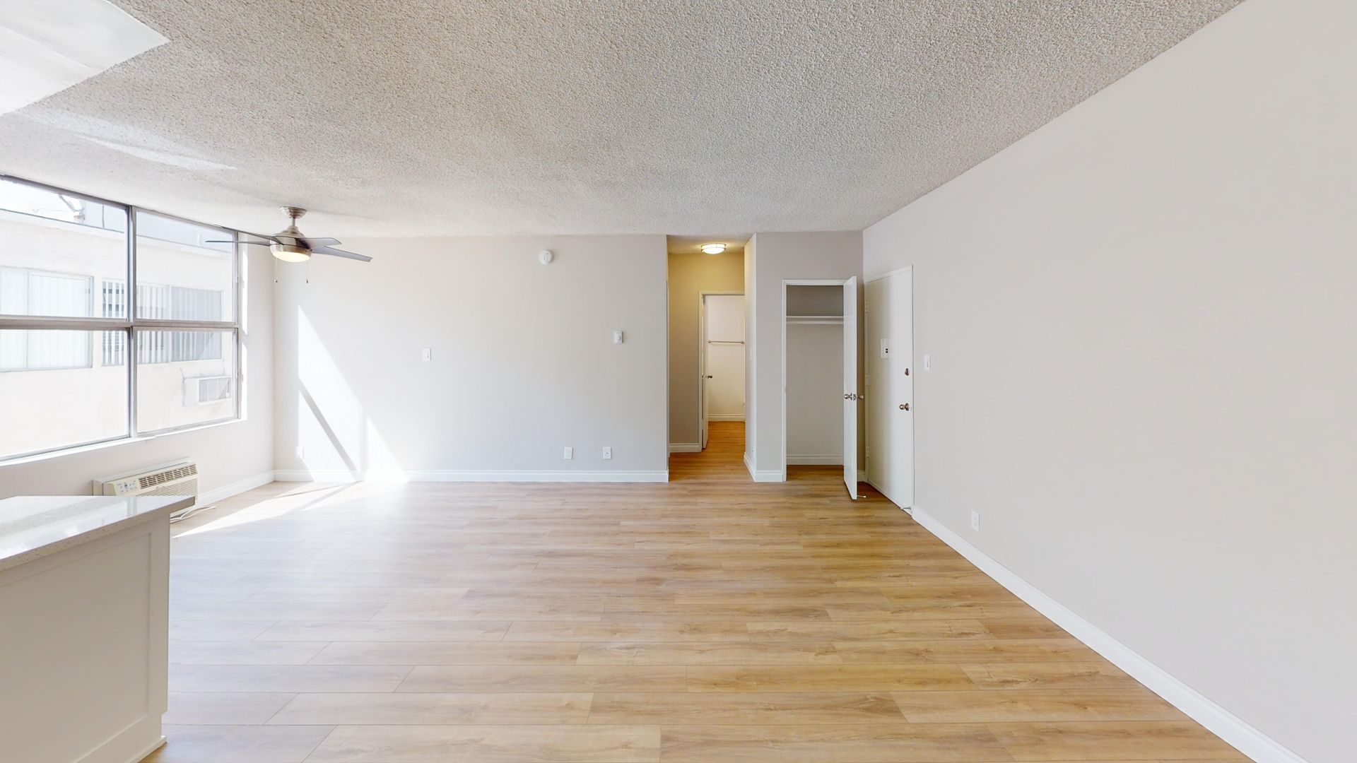 Empty apartment interior with light wood flooring, white walls, and a window.