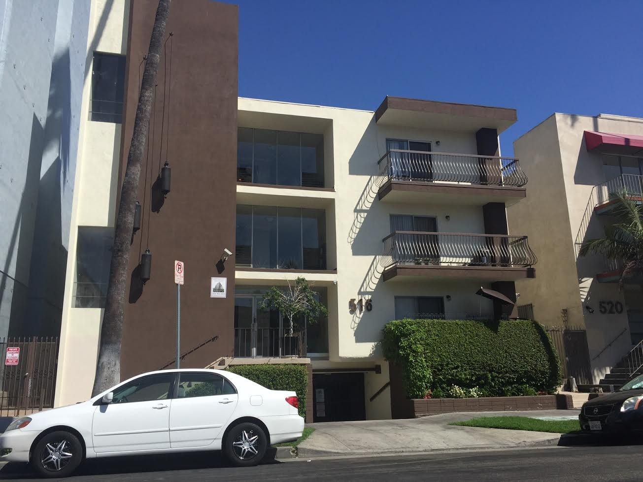 Apartment building with three stories, brown and beige facade. Entryway, car parked in front.