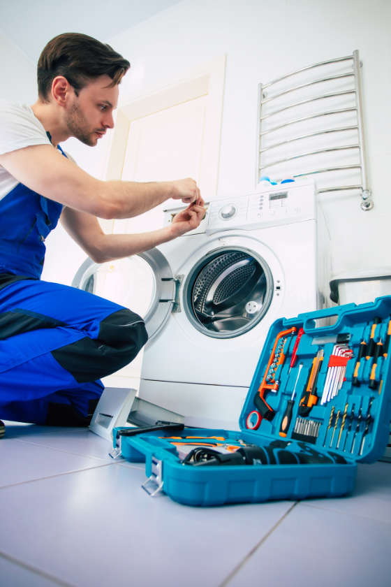 A man is kneeling on the floor fixing a washing machine.