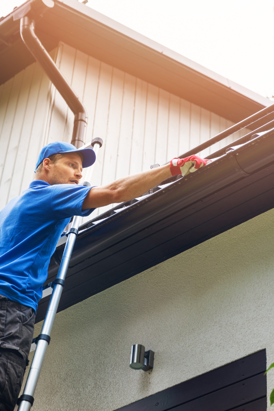 A man is standing on a ladder working on the gutters of a house.