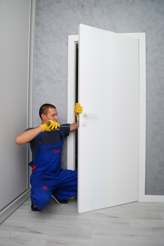 A man in blue overalls is kneeling down next to a white door.