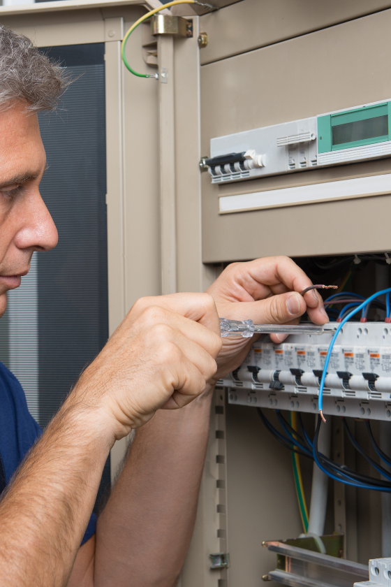 A man is working on an electrical box with a pair of pliers.
