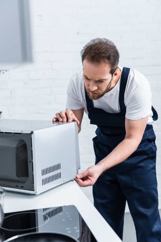 A man is fixing a microwave in a kitchen.