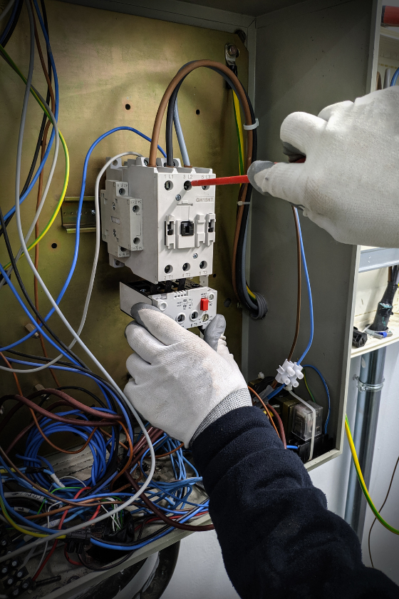 A person is working on an electrical box with a screwdriver.