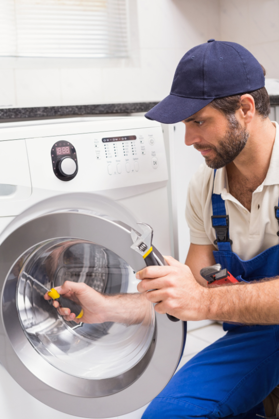 A man is fixing a washing machine with a screwdriver.