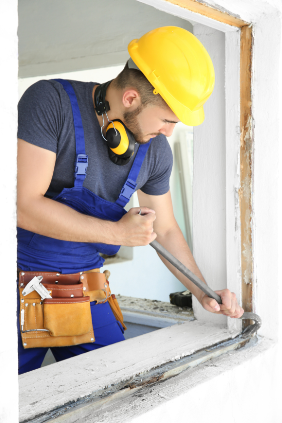 A man wearing a hard hat and headphones is working on a window frame.