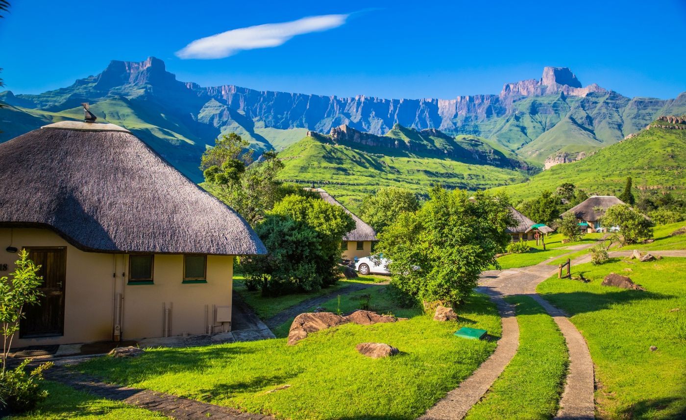 een rieten hut midden in een weelderig groen veld met bergen op de achtergrond in Zuid-Afrika