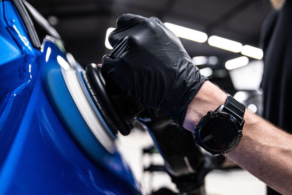 A man wearing black gloves is polishing a blue car.