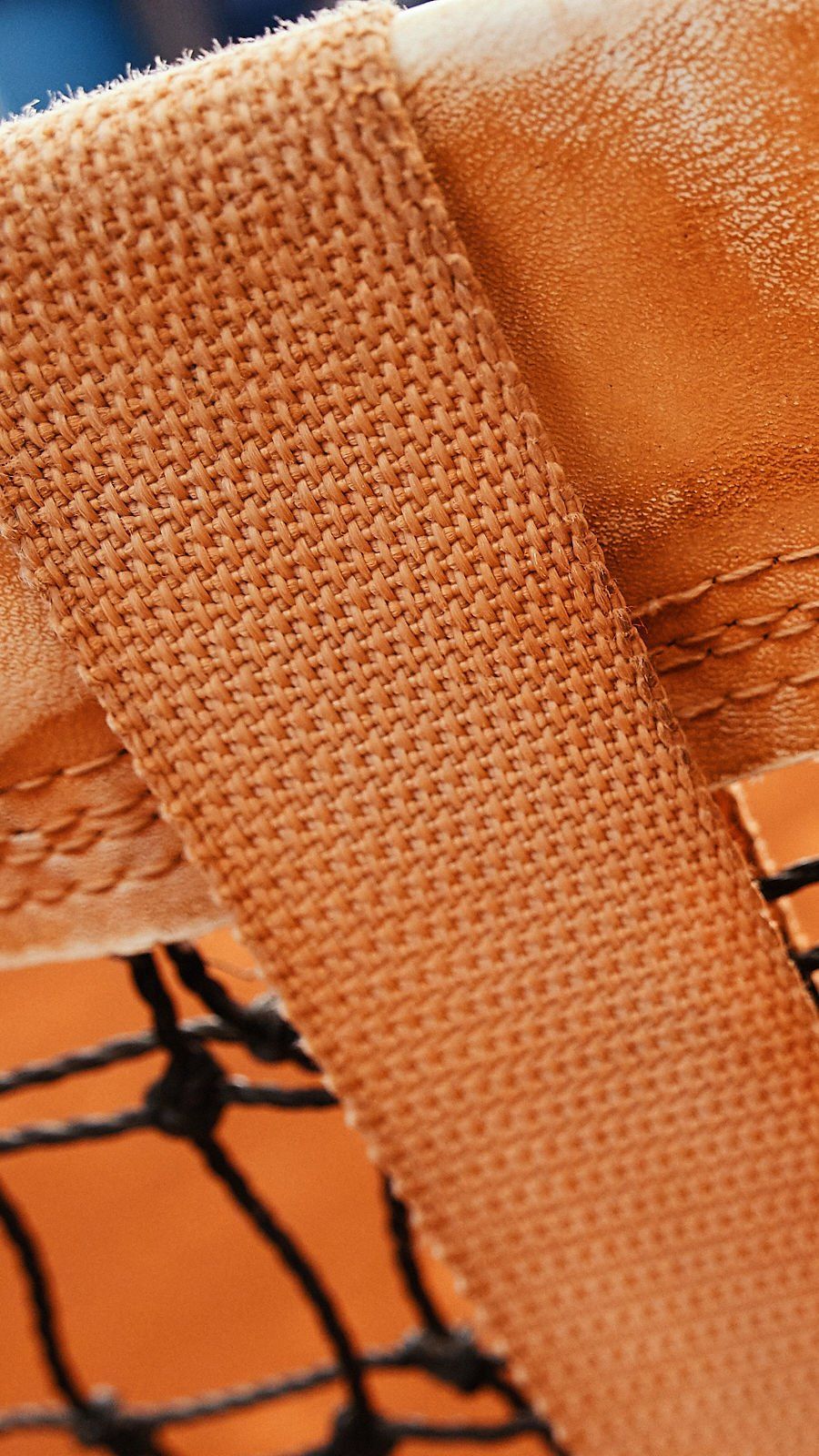 Close-up de tecido laranja da rede da quadra de tênis, com textura e costura visíveis.