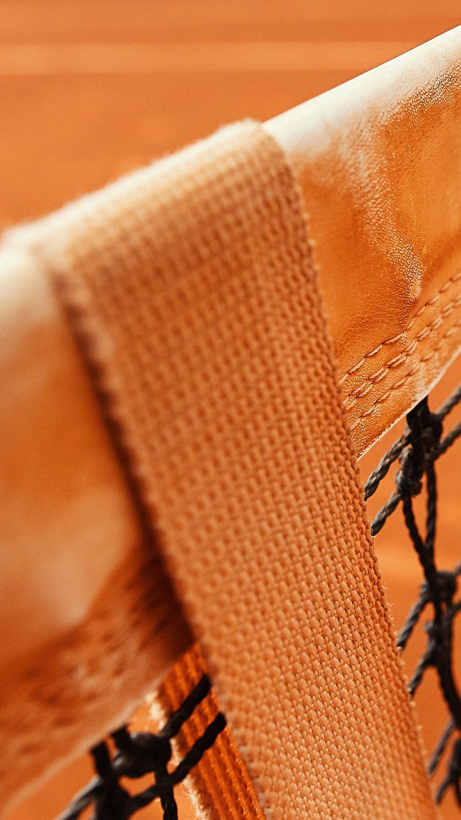 Close-up de uma rede de tênis com uma tira bege e um fundo de quadra de saibro.