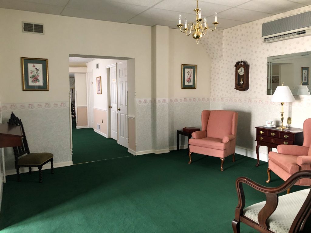 A living room with green carpet , chairs , a clock and a mirror.