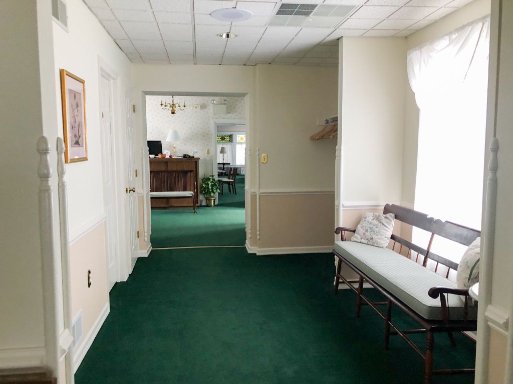 A long hallway with green carpet and a bench in the middle.
