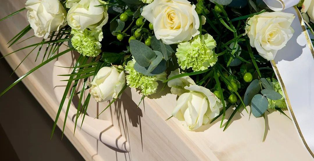 A coffin with white roses and green carnations on it.