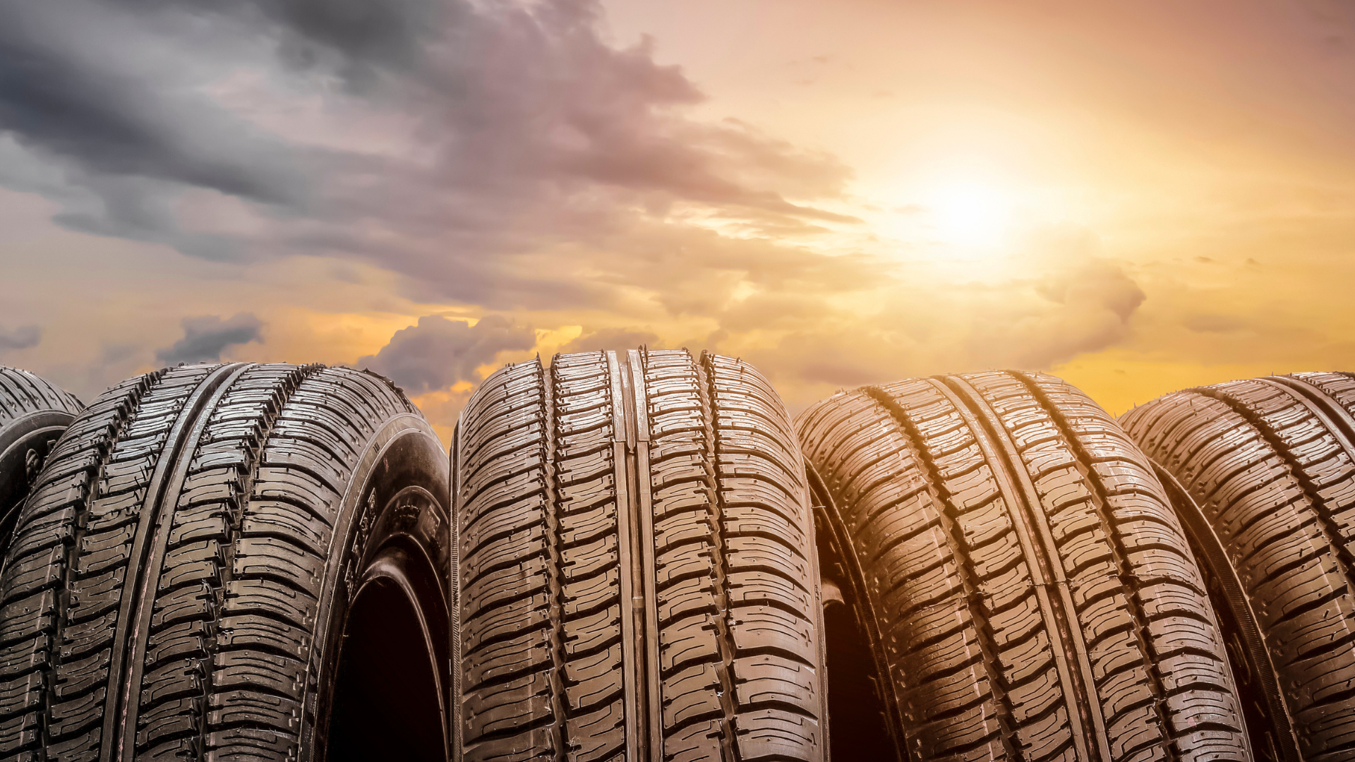 A row of tires are stacked on top of each other in front of a sunset.