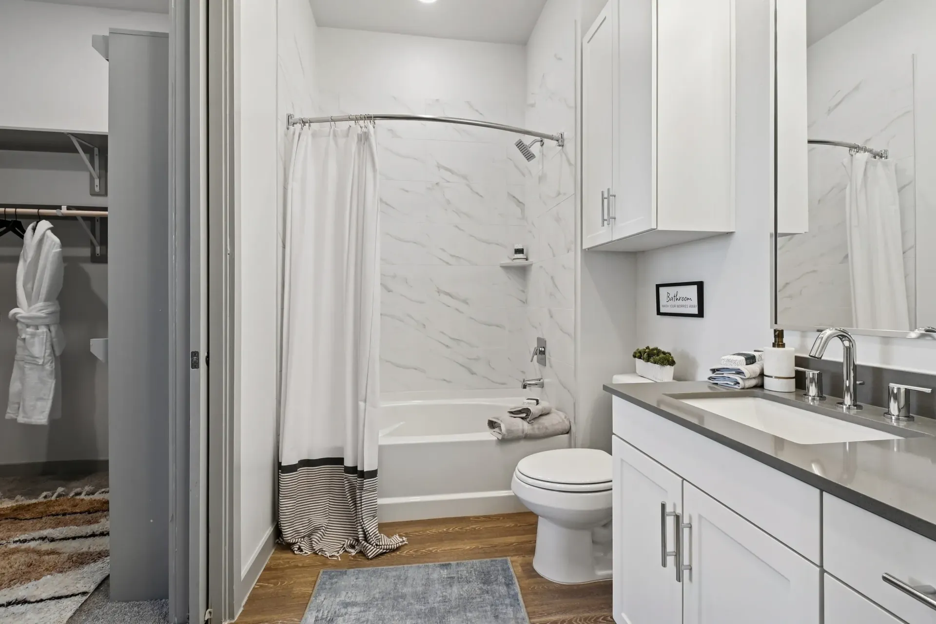 Modern white bathroom with marble-tile shower, shower curtain, toilet, and sink vanity.