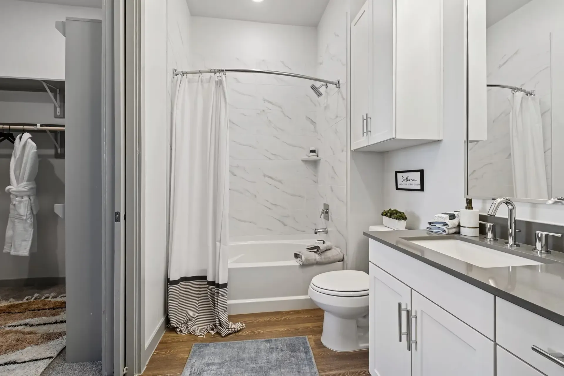 Bathroom interior with marble-tile shower, white cabinets, sink, and toilet.