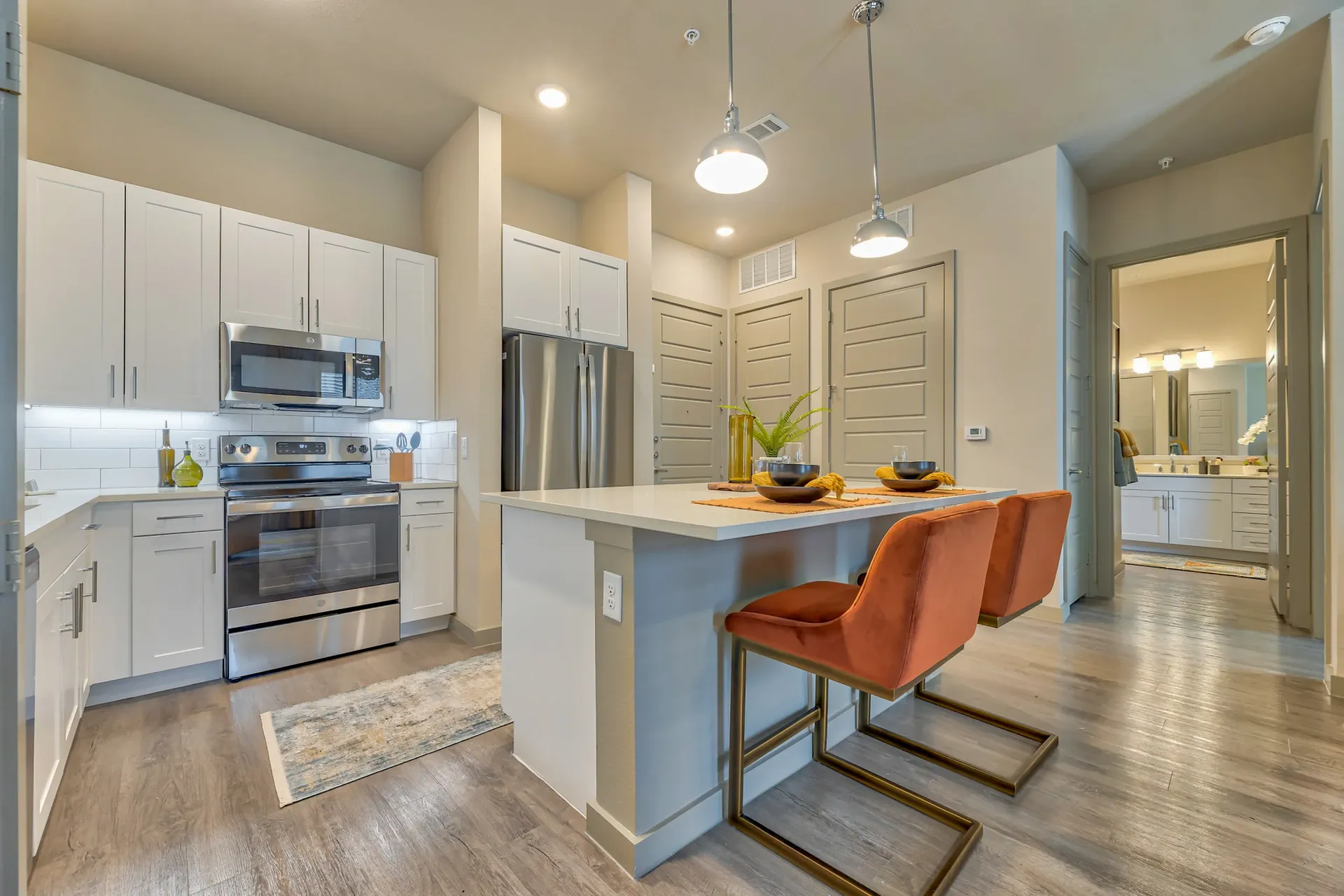 Modern apartment kitchen with white cabinets, stainless steel appliances, and an island with orange stools.