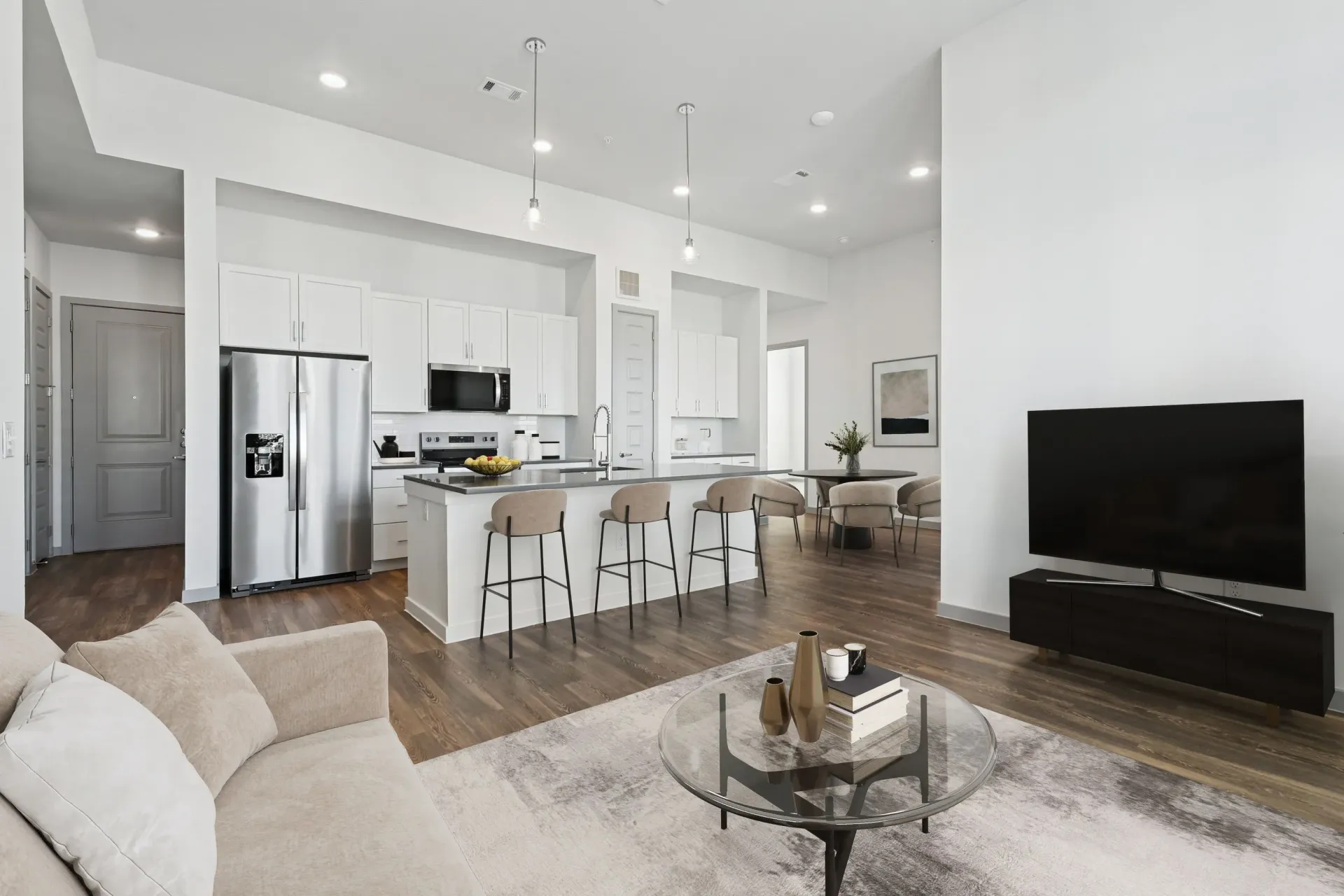 Open-concept kitchen and living area with white cabinets, stainless appliances, and a TV.