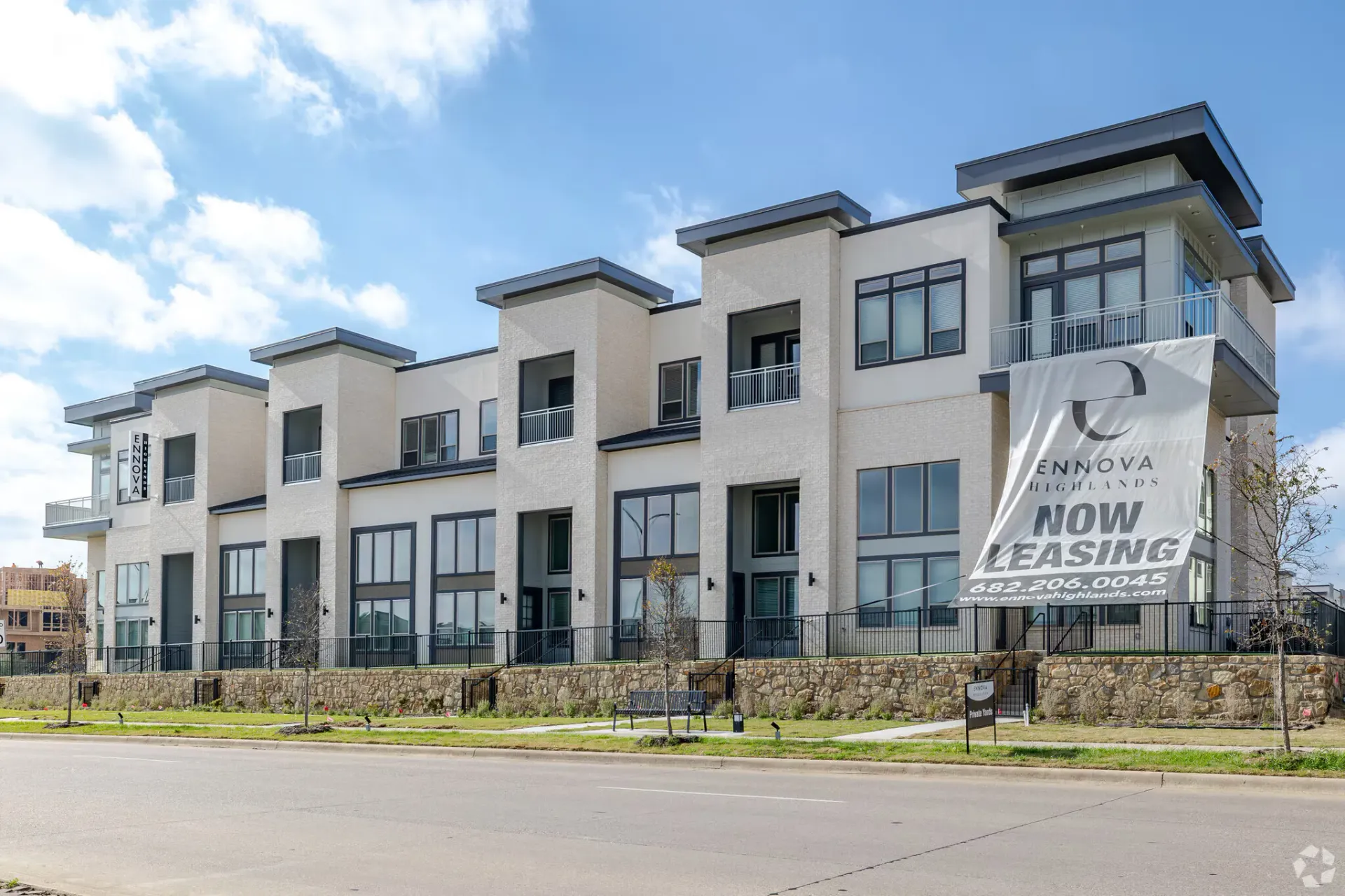 Exterior view of a modern multifamily building with a Now Leasing banner.
