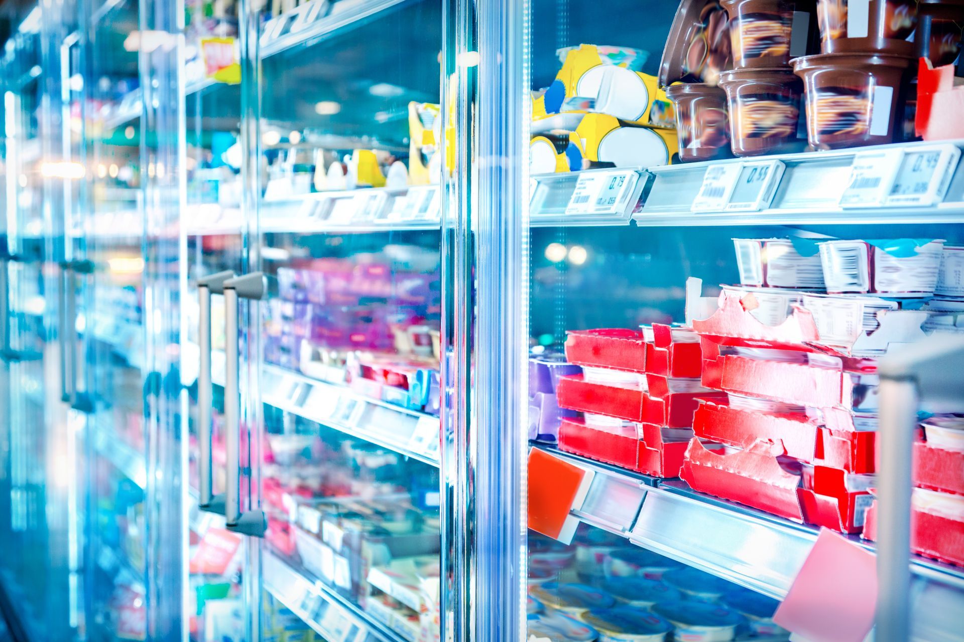 Refrigerator case in a grocery store, full of various packaged food items with glass door.
