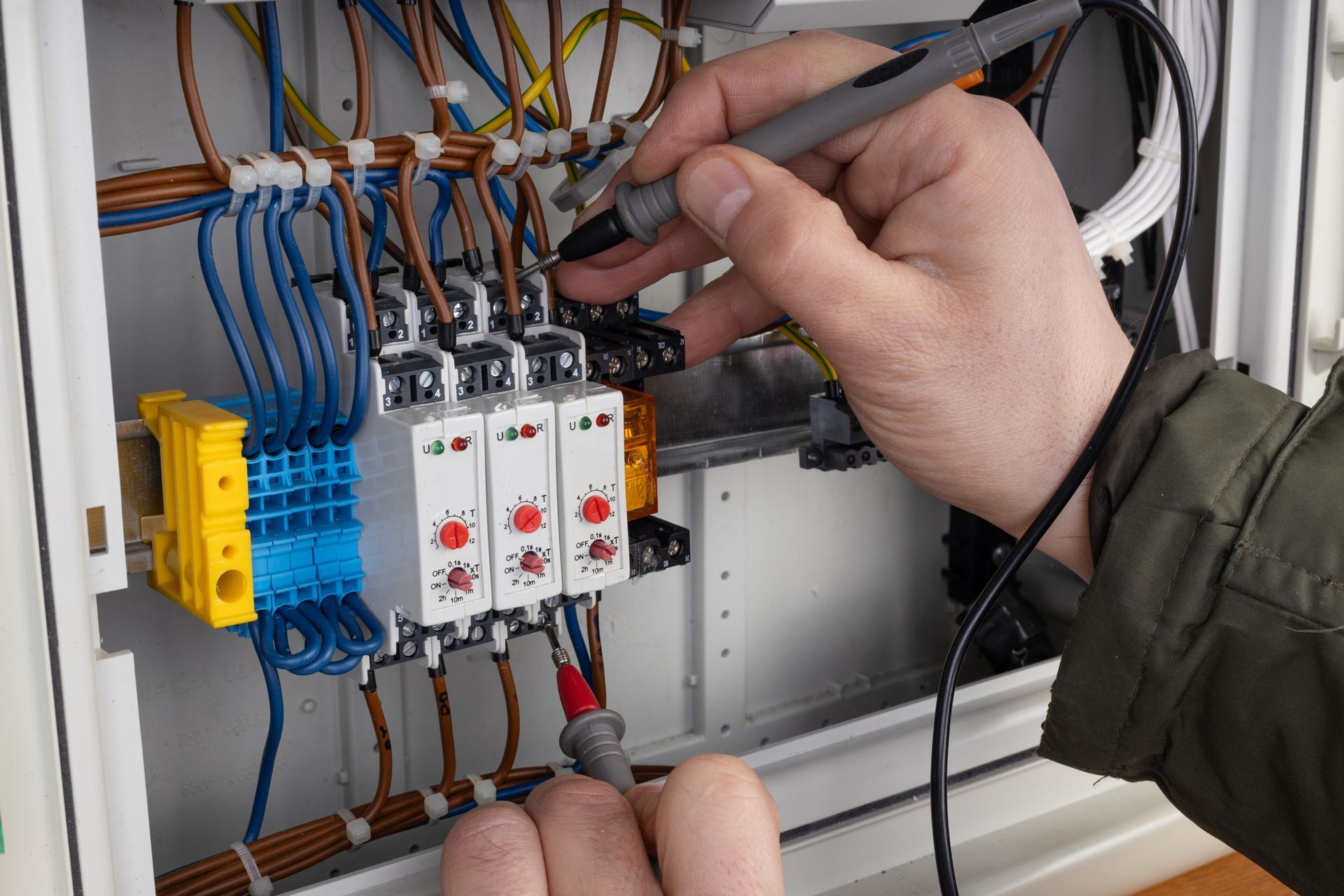 Electrician testing wires in a control panel with a multimeter.