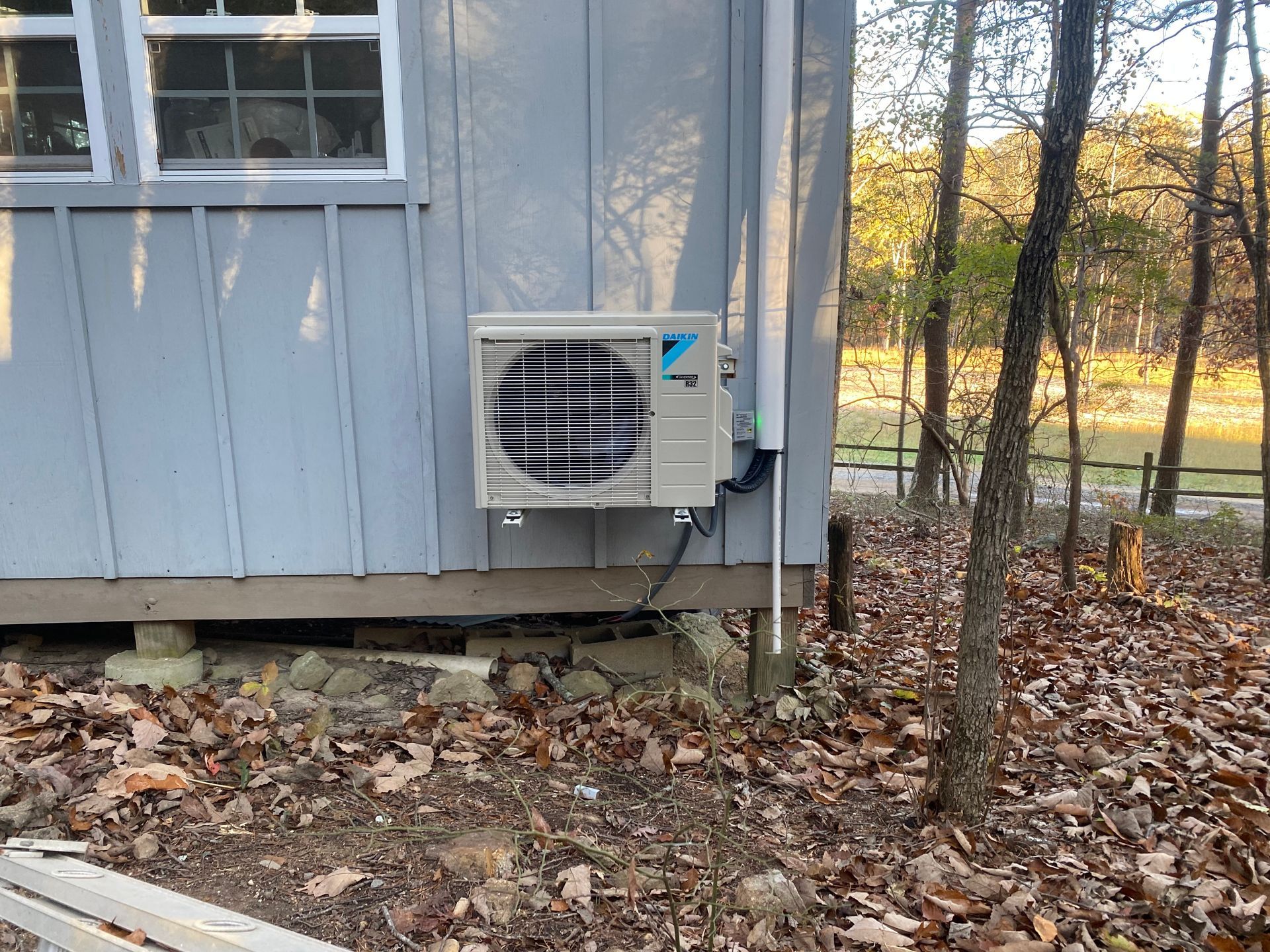 A white air conditioner is sitting on the ground next to a wooden fence.