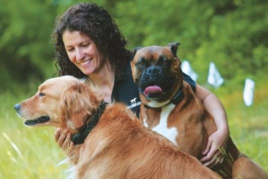A Dogwatch service provider woman is sitting in the grass with two dogs.