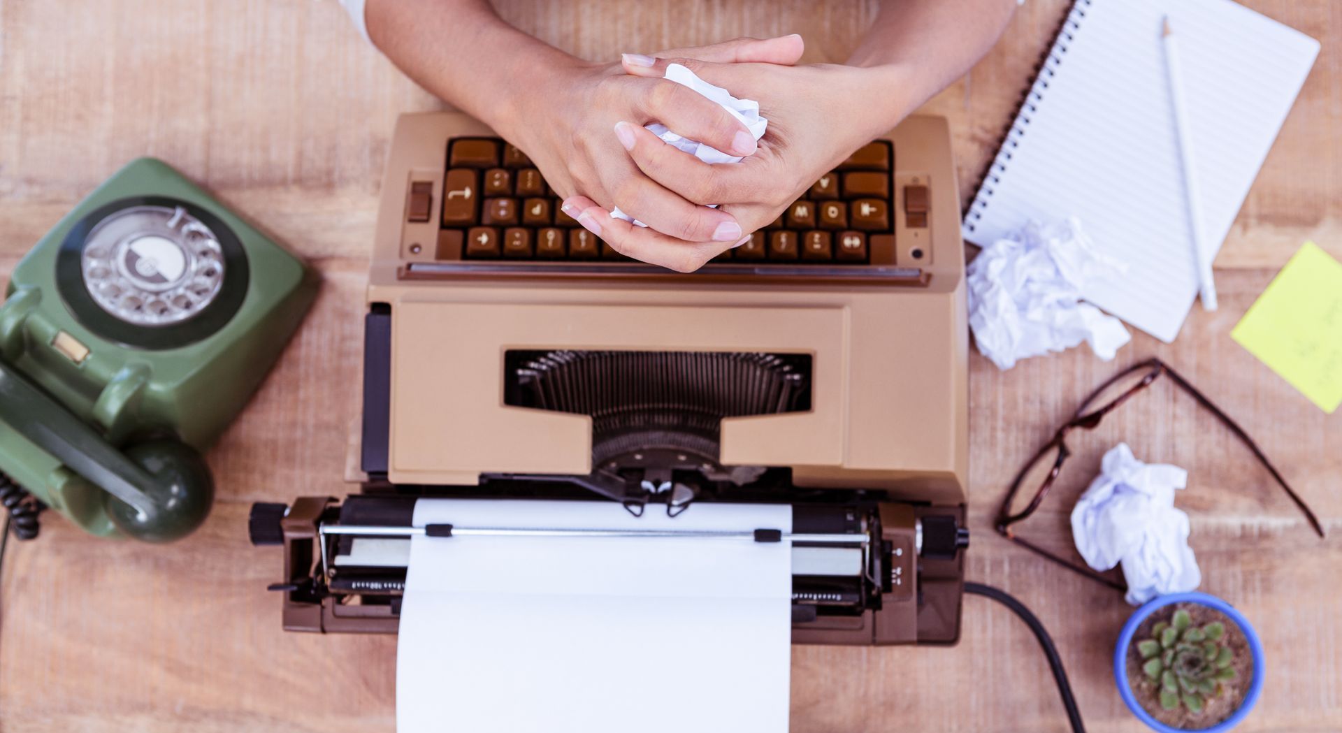 A person is typing on an old typewriter on a wooden desk.