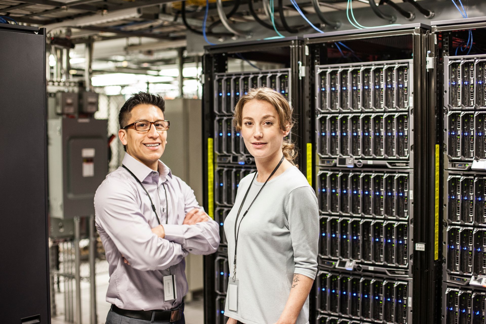 A man and a woman are standing next to each other in a server room.