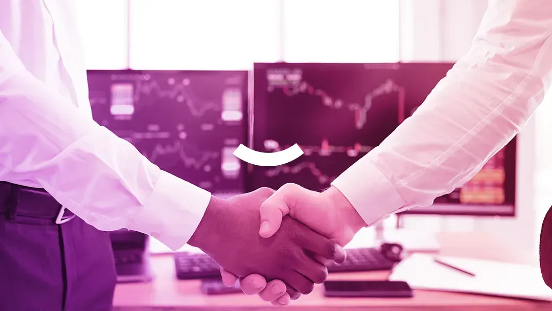 Two people are shaking hands in front of a computer screen.