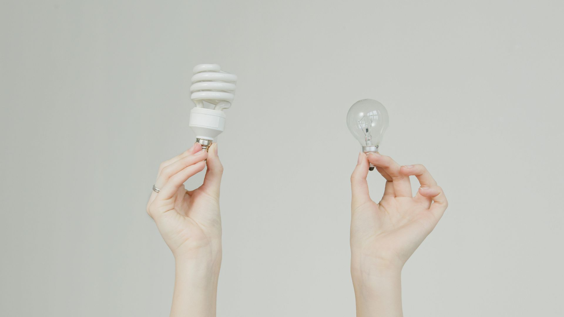 Two hands holding a compact fluorescent bulb and an incandescent bulb against a gray background