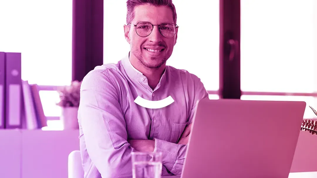A man is sitting at a desk with his arms crossed in front of a laptop computer.