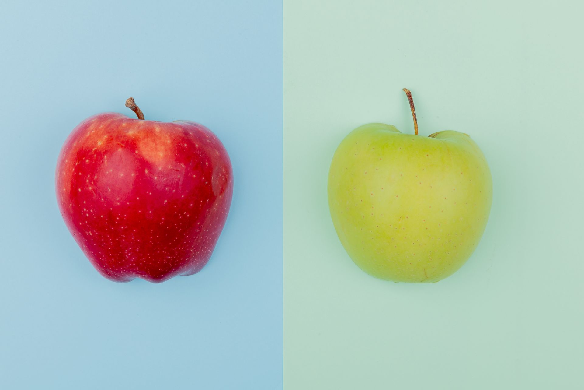 Red and yellow apples side by side on pastel blue and green backgrounds.