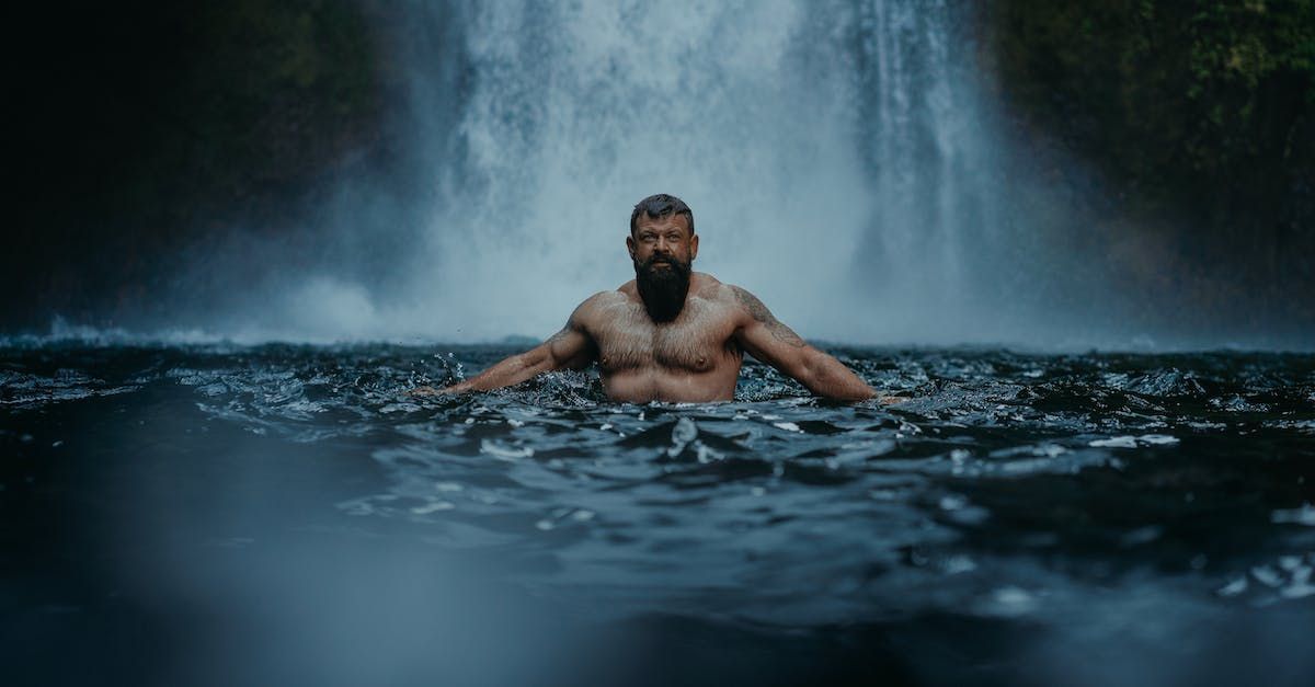 Een man met een baard zwemt in een waterval.