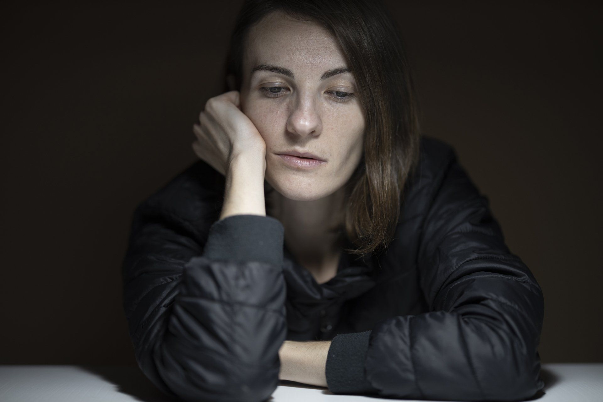 Een vrouw zit aan een tafel met haar hoofd op haar hand.