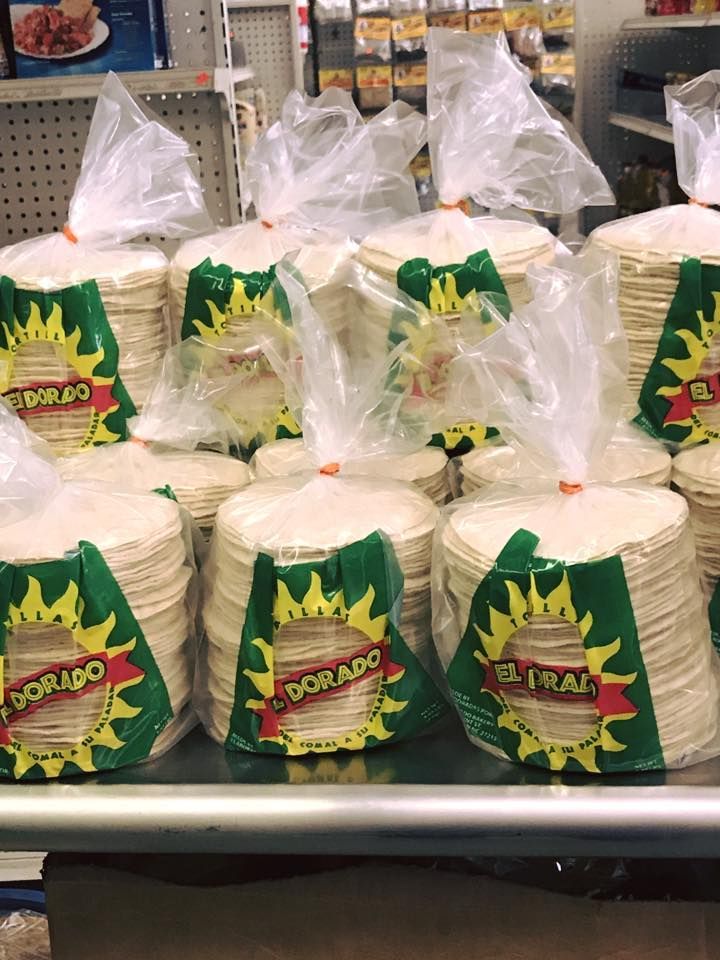 A stack of round flour tortillas on a piece of brown parchment paper against a dark wood background.