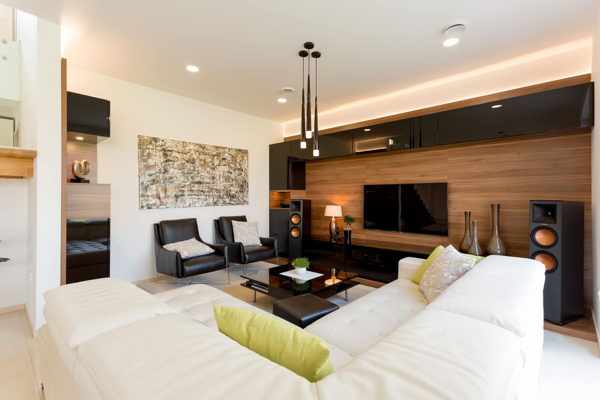 Modern living room with white sectional sofa, wood paneling, black accents, and a large television.