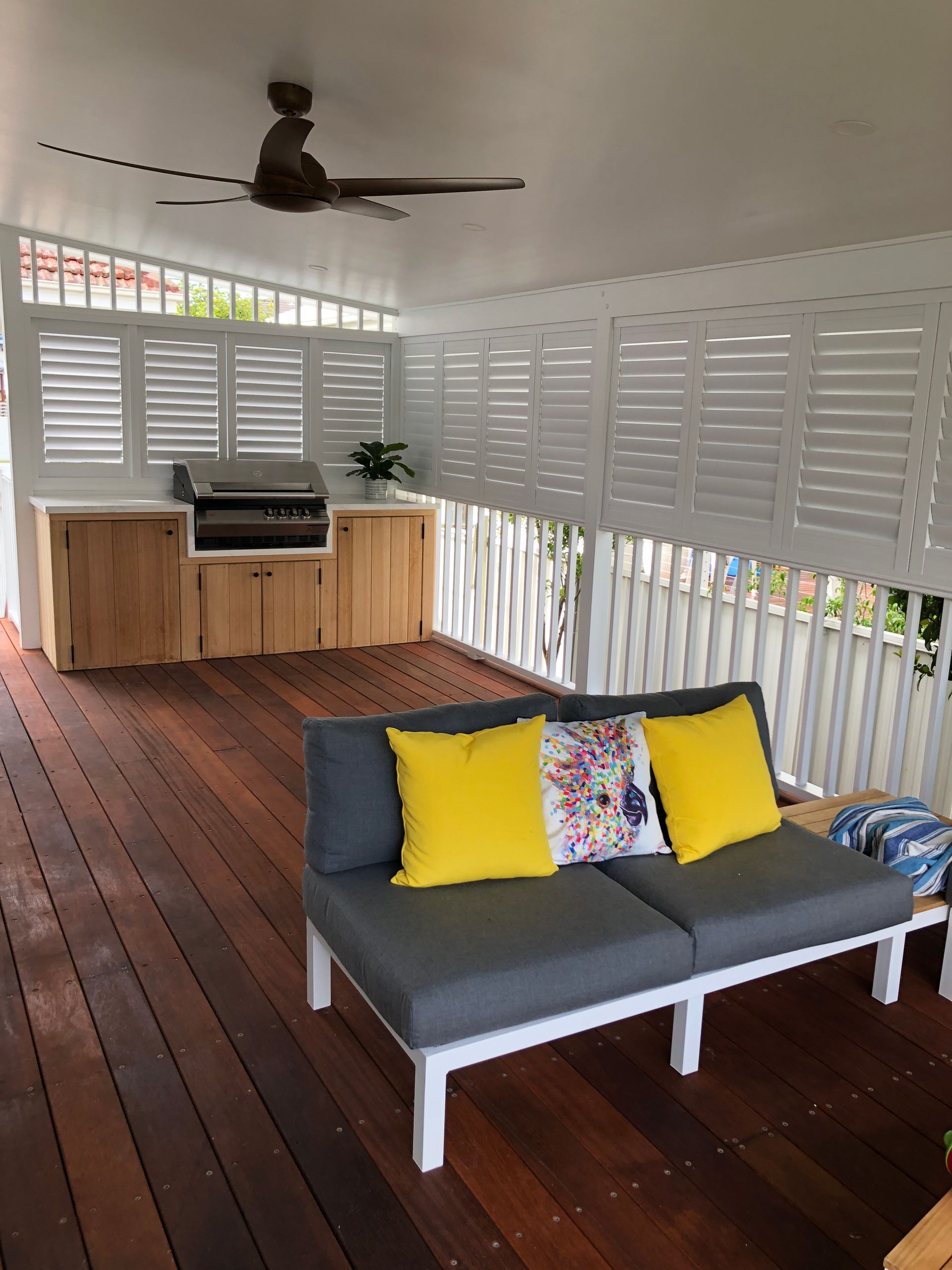 Outdoor Deck With Gray Couch, Yellow Pillows, Grill, and White Shutters — My Timber Flooring Blinds & Shutters in Erina, NSW