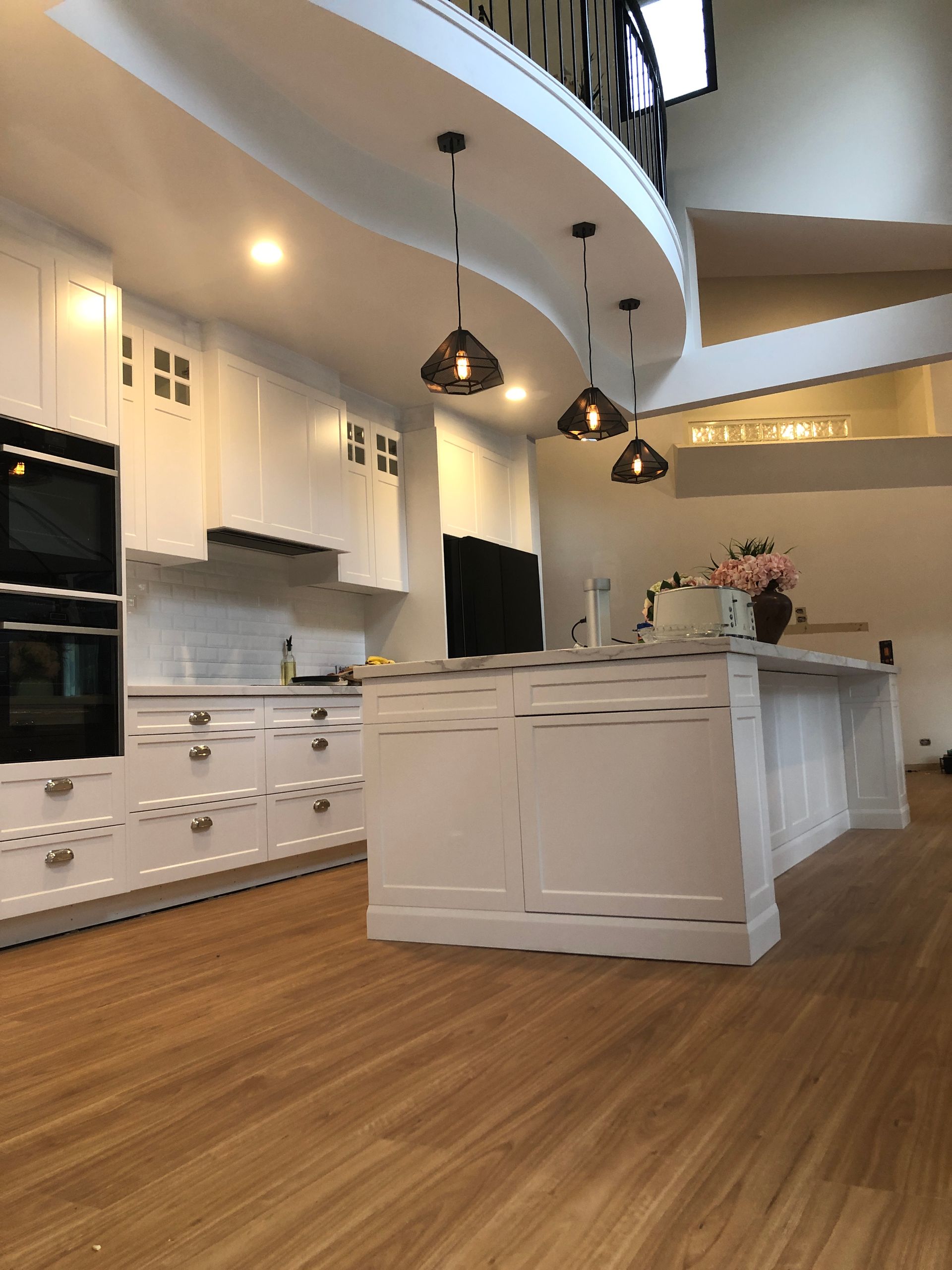 White kitchen with island, cabinets, oven, range hood, and pendant lights. Wooden floor.— My Timber Flooring Blinds & Shutters in Erina, NSW